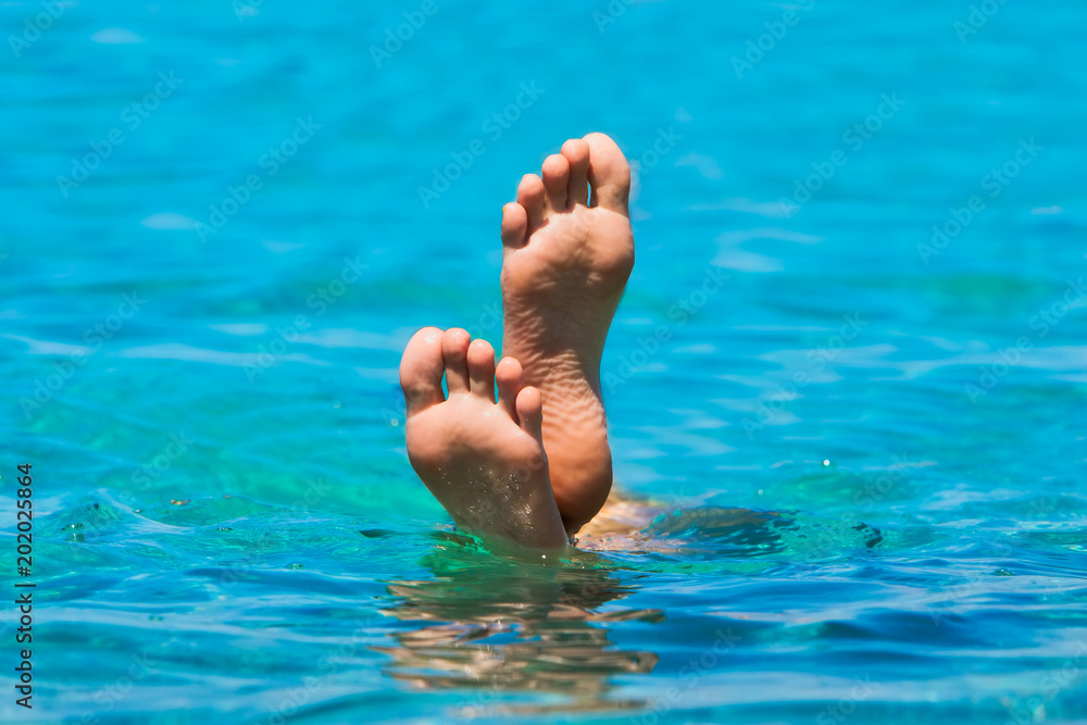 The feet that emerge from the sea water on a paradisiacal beach. Holiday.
