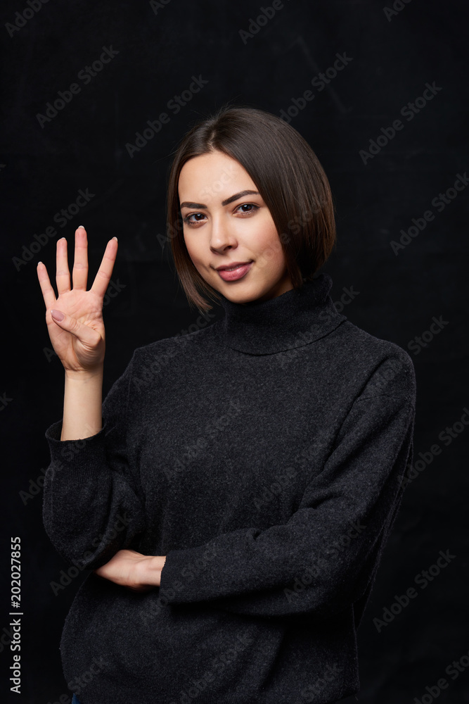 Hand counting - four fingers.Smiling woman in grey turtleneck sweater over dark background showing four fingers Hand counting - four fingers.Smiling woman in grey turtleneck sweater over dark background showing four fingers