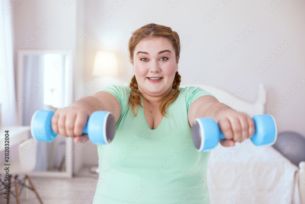 Joyful time. Happy red-head woman smiling while holding weights Joyful time. Happy red-head woman smiling while holding weights