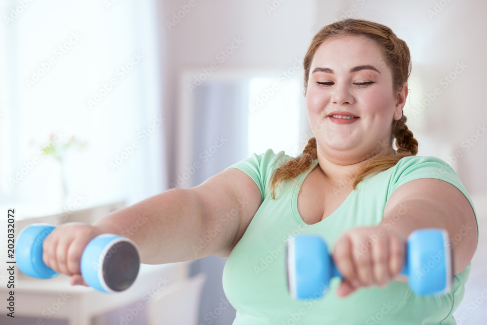 Sports program. Smiling young woman doing exercises with dumbbells while watching sports program Sports program. Smiling young woman doing exercises with dumbbells while watching sports program