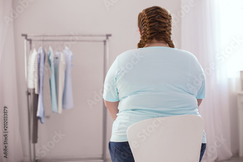New clothes. Overweight young woman sitting on the chair while thinking about new clothes photo