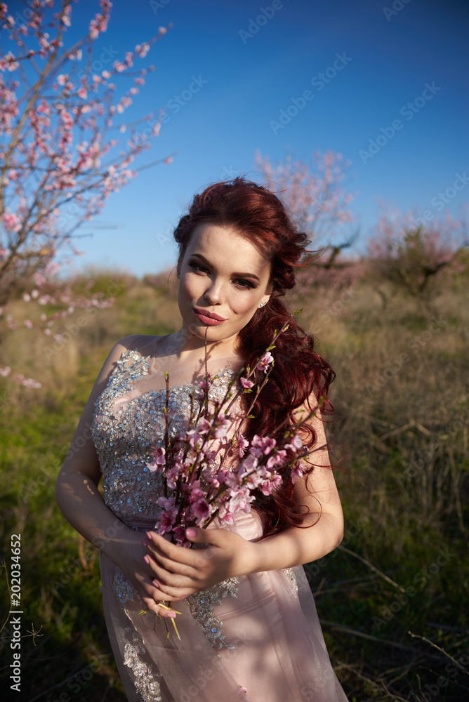 Naklejka premium Young woman in a dress walking among peach trees