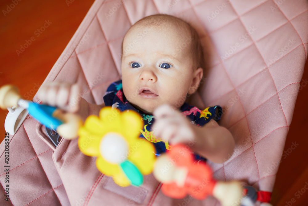 Baby girl sitting in bouncer and playing with colorful toys Baby girl sitting in bouncer and playing with colorful toys