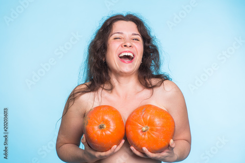 Young happy woman holds pumpkin in hands above her breast. Plastic surgery and silicone implants concept. photo