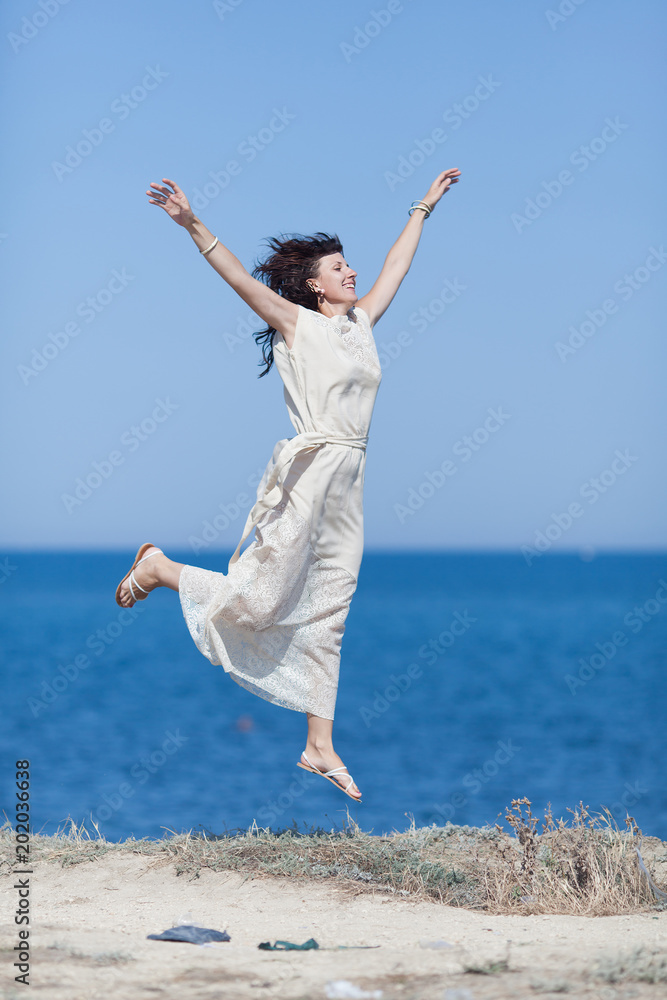 Middle aged woman jumping against sea with arms raised Middle aged woman jumping against sea with arms raised