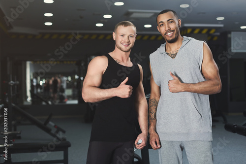 Muscular men showing thumbs up at camera at gym