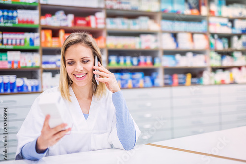 Portrait of a young friendly female pharmacist with smartphone.
