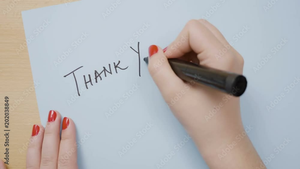 Woman hands with red nail polish writing thank you on a blue paper with a black marker Woman hands with red nail polish writing thank you on a blue paper with a black marker