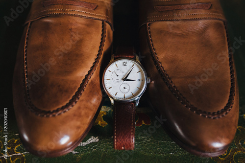 The wrist watch is next to the men's leather shoes