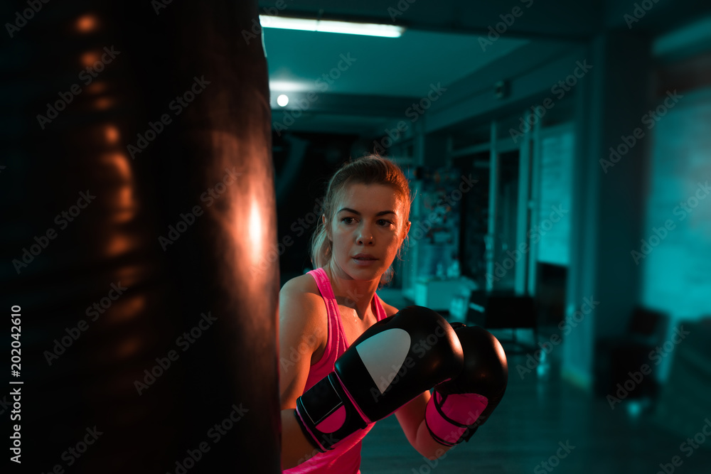 Beautiful woman training with punch bag in the gym at night