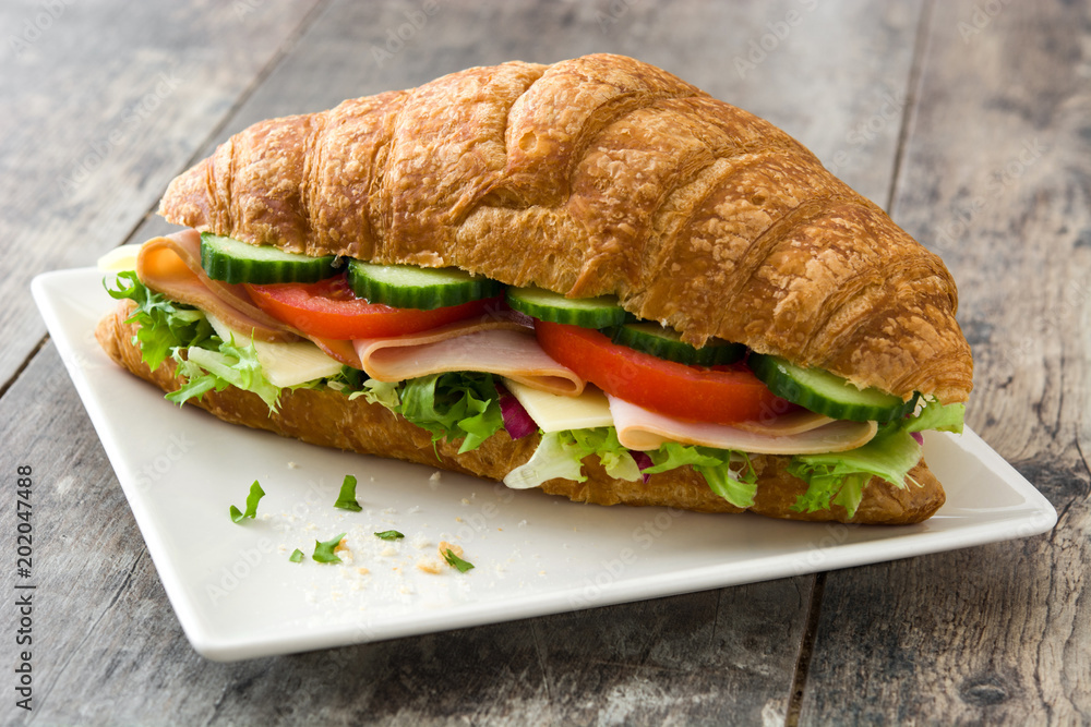 Croissant sandwich with cheese, ham and vegetables on wooden table Croissant sandwich with cheese, ham and vegetables on wooden table