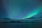 Northern light aka Aurora Borealis glowing on sky in Jokulsarlon glacier lagoon with snow capped mountains in background at night in Iceland