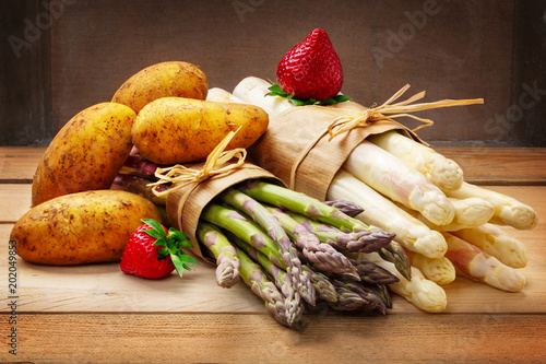Asparagus, strawberries and potatoes on wooden board photo