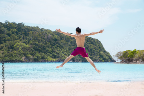 Happy young man jumping on the beach at the day enjoying of his summer holiday