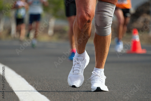 Senior run marathon with knee bandage, running in the light of evening,detail of sports shoes
