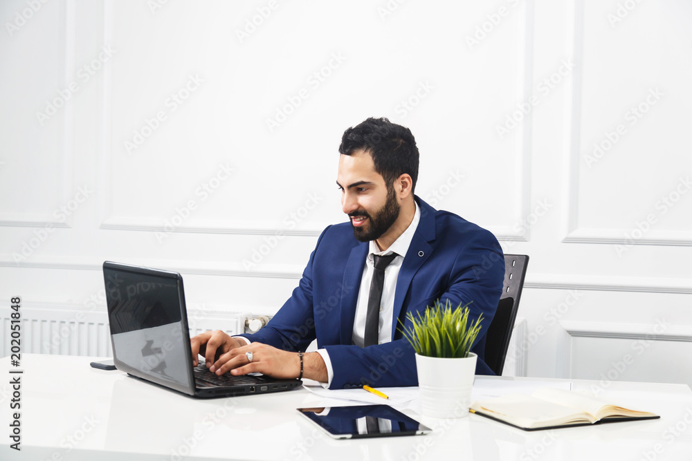 Bearded businessman dressed in blue suit work with laptop in white office interior Bearded businessman dressed in blue suit work with laptop in white office interior