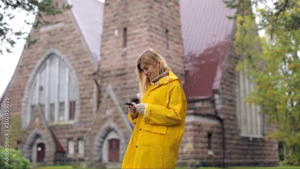 woman in a yellow raincoat with phone near an old church