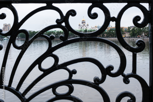 Black cast ornate lattice of city embankment fence of Yekaterinburg with view of the Temple on Blood through it.