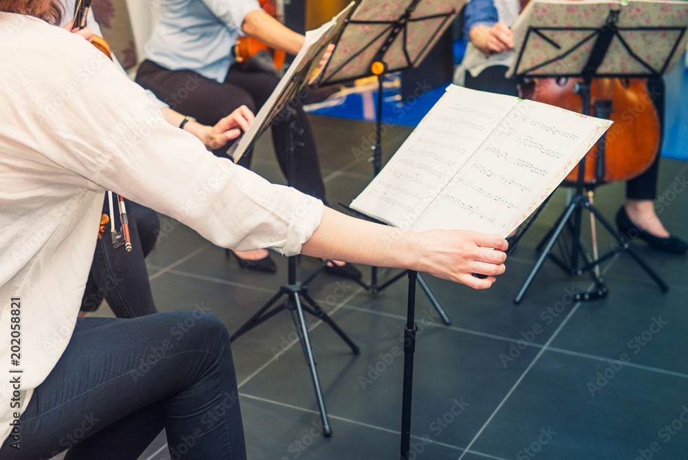Obraz premium Musician turn the page of Music notebook on stand with background of playing cellists and violinists band on event. Commercial music. Service at business meeting, party, weddings.