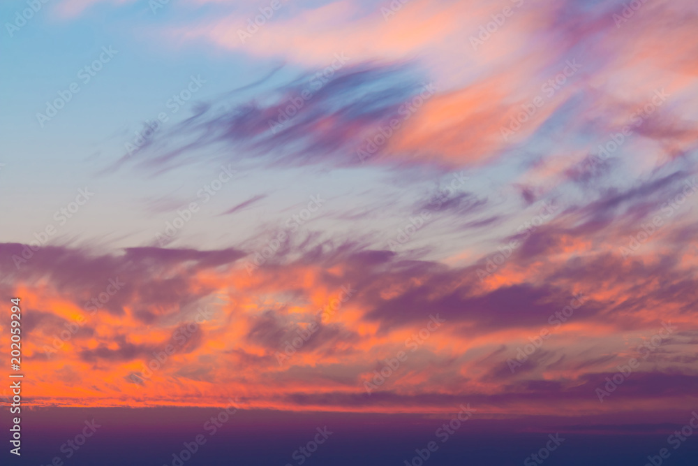 Beautiful cloudscape at scarlet sunset with colorful contrasting cirrus clouds
