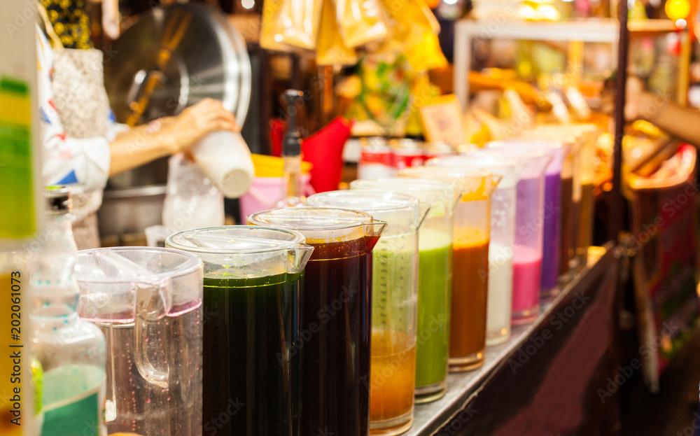 Colorful Cold Thai Milk Ice Tea in jugs on the street food market stall. Traditional Thai Beverage made with milk, sugar and tea.
