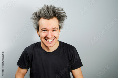 Принти на полотні Unshorn and unshaven young guy with piercings on his face with wide smile on gray background