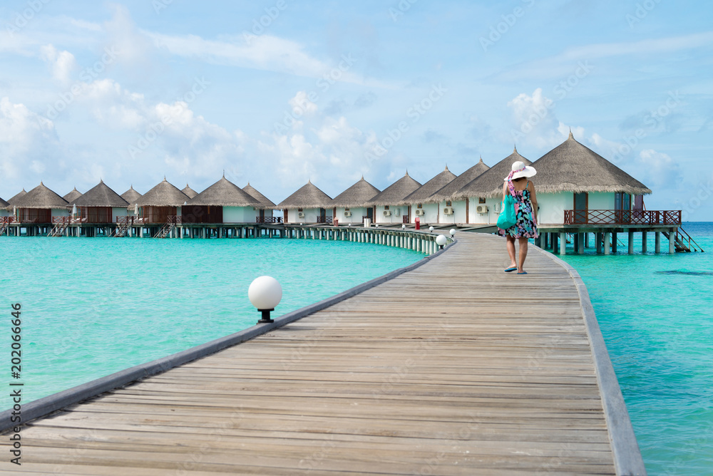 A woman traveler walking alone on wooden planks in the Maldives island on the background of a bungalow on the water and the beauty of the sea with the coral reefs