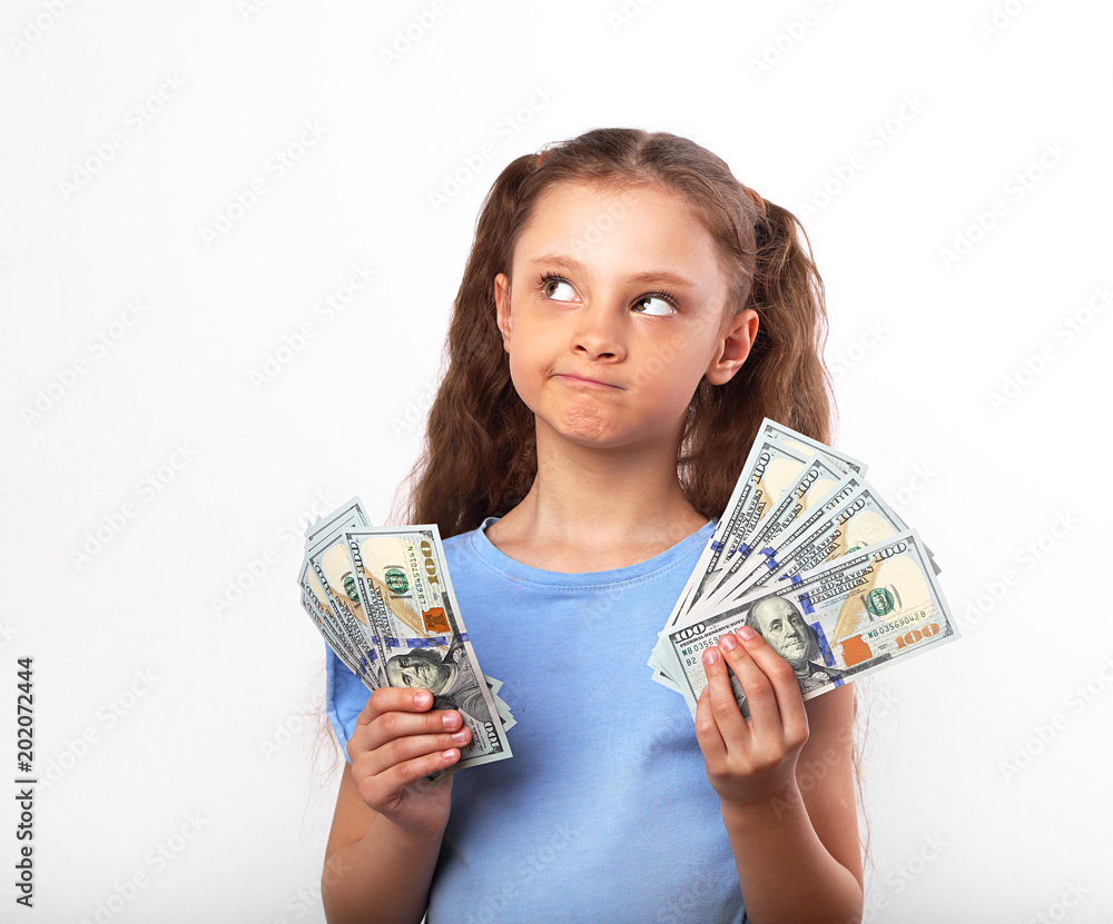 Happy grimacing doubt thinking kid girl holding money in the hands and looking up on white background with empty copy space Happy grimacing doubt thinking kid girl holding money in the hands and looking up on white background with empty copy space