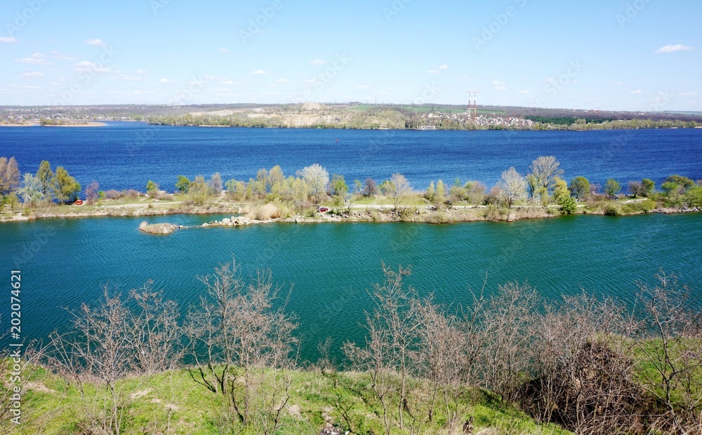A view of the lake with turquoise water and a river with dark blue water from a hill. They share a thin strip of land on which people like to rest.