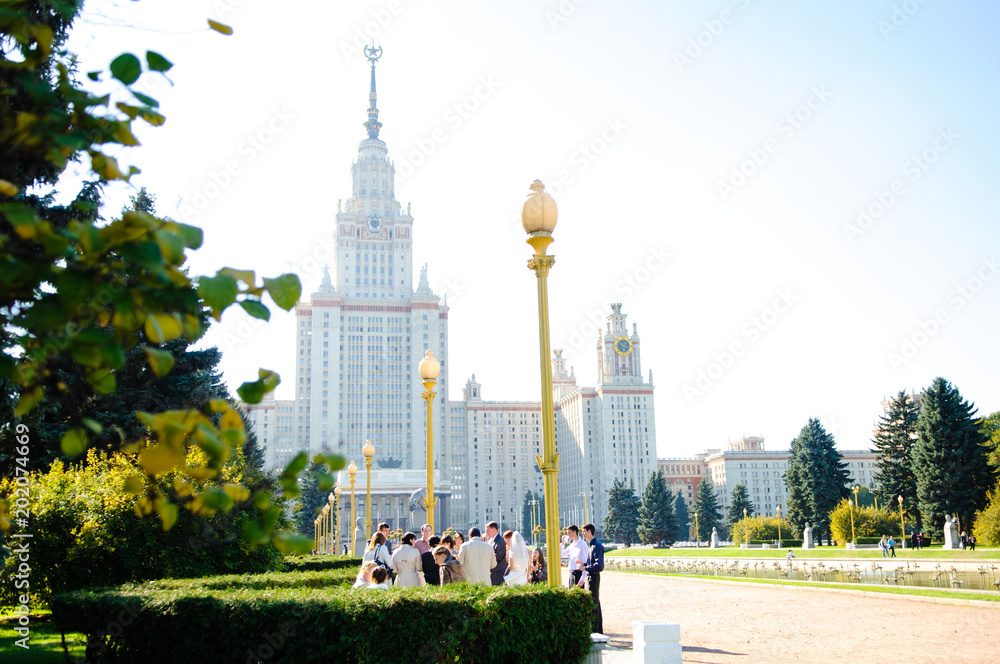 Obraz premium Newlyweds with guests on a walk on the wedding day near the building of the Moscow State University.