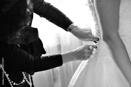 Women s hands tie a ribbon on the corset of a wedding dress. Morning gathering of the bride. Black and white.