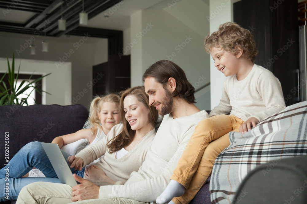 Happy family with children talking using laptop on couch at home, smiling couple doing online shopping choosing planning with kids on weekend, parents and son daughter relaxing on sofa with computer Happy family with children talking using laptop on couch at home, smiling couple doing online shopping choosing planning with kids on weekend, parents and son daughter relaxing on sofa with computer