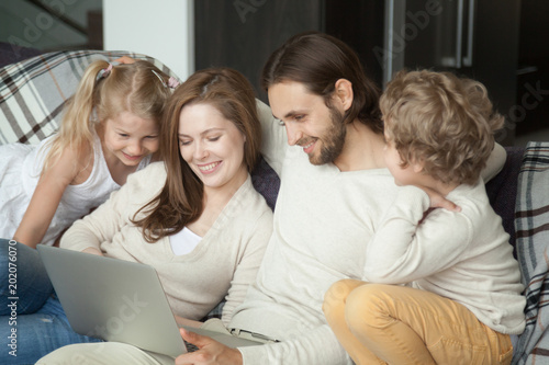 Smiling parents with kids using laptop on sofa, happy family with children son daughter having fun with computer doing online shopping or watching funny video together sitting on couch at home