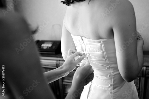 Women's hands tie a ribbon on the corset of a wedding dress. Morning gathering of the bride. Black and white.