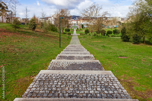 Empty cobblestone path, track, trail or pathway through the trees and green grass lawn in Parque da Devesa Urban Park. City of Vila Nova de Famalicao, Portugal, in background photo