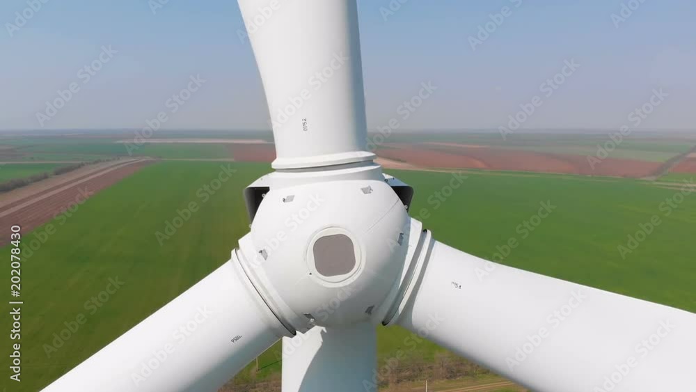 Aerial view of a rotating wind generator in a green field during the day. Electricity generation. The drone flies by next to the turbine. The windmill is close-up. Modern technologies. Aerial view of a rotating wind generator in a green field during the day. Electricity generation. The drone flies by next to the turbine. The windmill is close-up. Modern technologies.