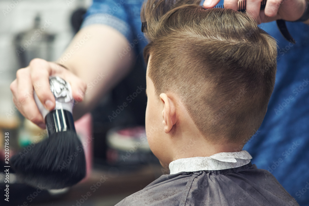 Hairdresser making a hairstyle to a boy in barbershop.