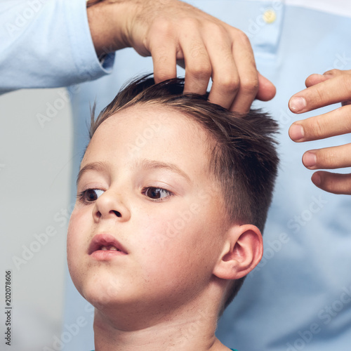 Barber is making a hairstyle to Caucasian boy in barbershop.