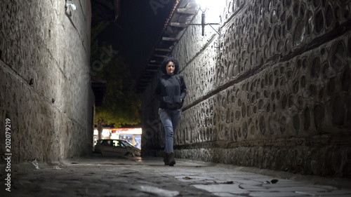 Woman in jeans and boots walk in Dark Urban Alley at Night, cinematic low angle shot