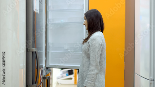 Young woman in a home appliance shop chooses a refrigerator