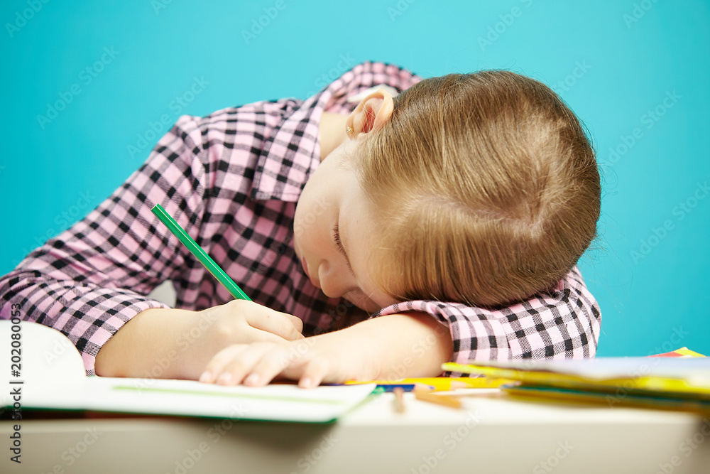 Isolated shot of child with poor posture sitting at desk and do homework. Girl rested her head on table and writes in notebook. Isolated shot of child with poor posture sitting at desk and do homework. Girl rested her head on table and writes in notebook.