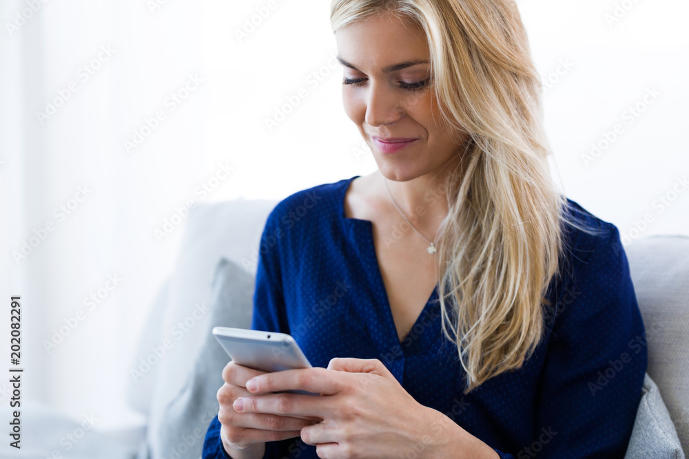 Pretty young woman using her mobile phone while sitting on sofa at home. Pretty young woman using her mobile phone while sitting on sofa at home.