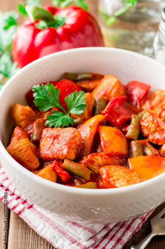 Turkey stew with bell peppers, green beans and tomatoes in bowl on dark wooden table