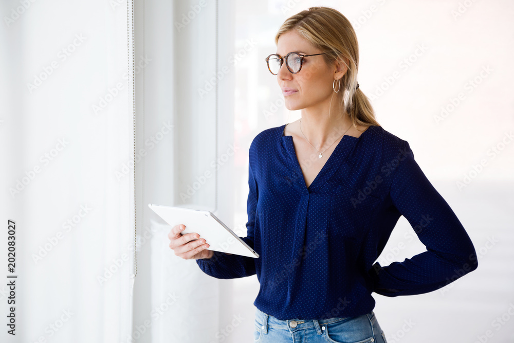 Pretty young woman looking sideways while using her digital tablet at home.