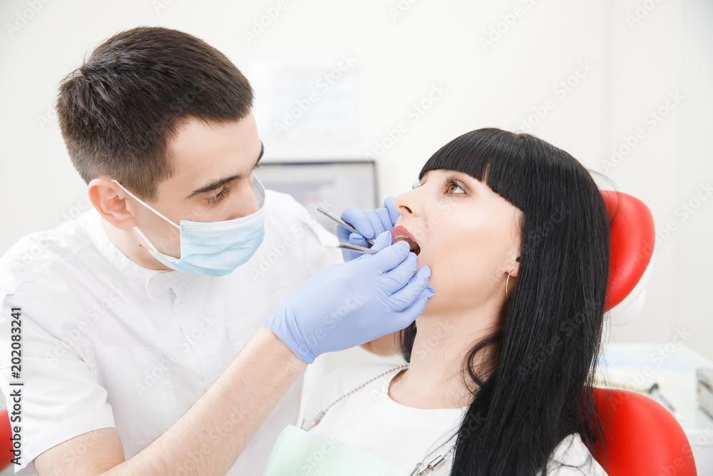Male dentist examines, checks condition teeth of young woman of patient.