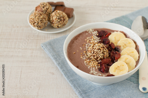 Chocolate hazelnut smoothie bowl topped with sliced banana, goji berries,   sesame seeds and dates oatmeal energy balls
