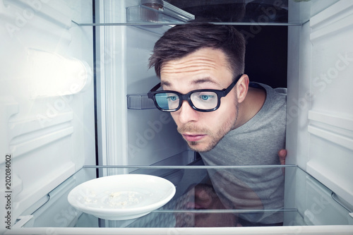 Fotografiet Student schaut in einen leeren Kühlschrank
