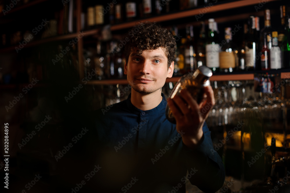 Young curly barman shaking a fresh summer cocktail in a shaker
