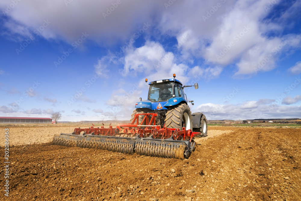 Fototapeta premium modern farmer with tractor cultivating the field at sunset