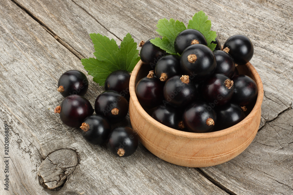 black currant in wooden bowl with green leaf on old wooden background black currant in wooden bowl with green leaf on old wooden background